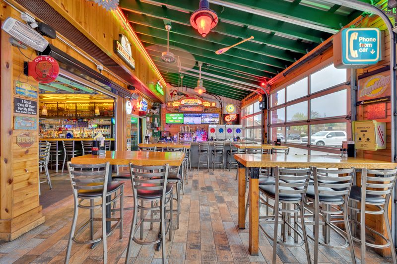 Inside Clarkston Tap: long wooden high-tops, neon signs, the back bar and glass garage doors along the patio side