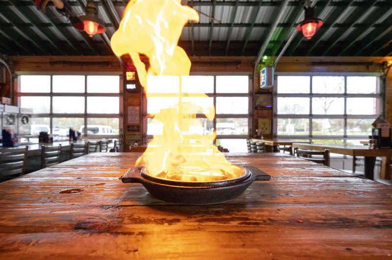 Saganaki cheese flaming in a skillet on a wooden table, garage doors behind